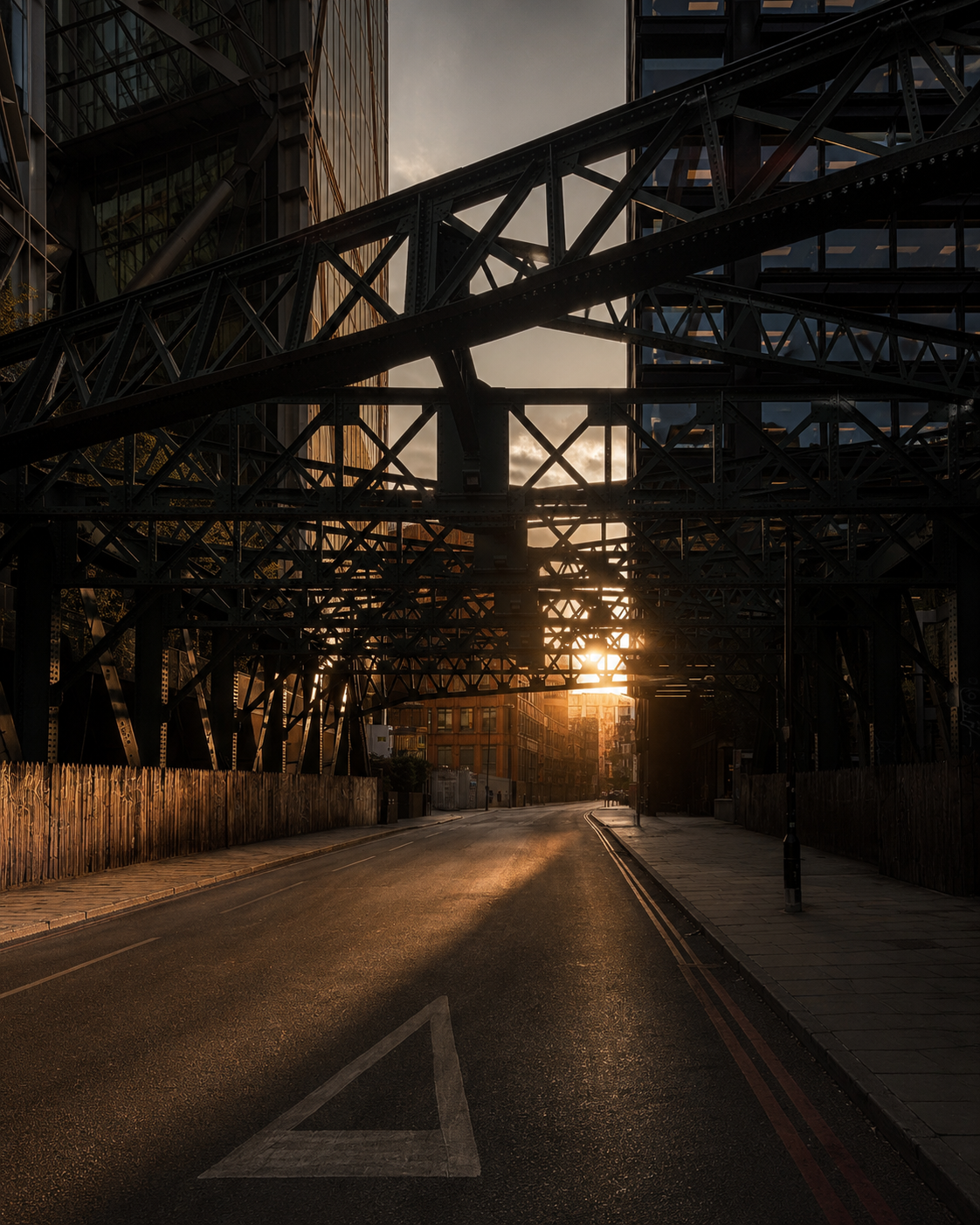 Sunset seen through an old riveted steel bridge crossing an empty London street between modern towers
